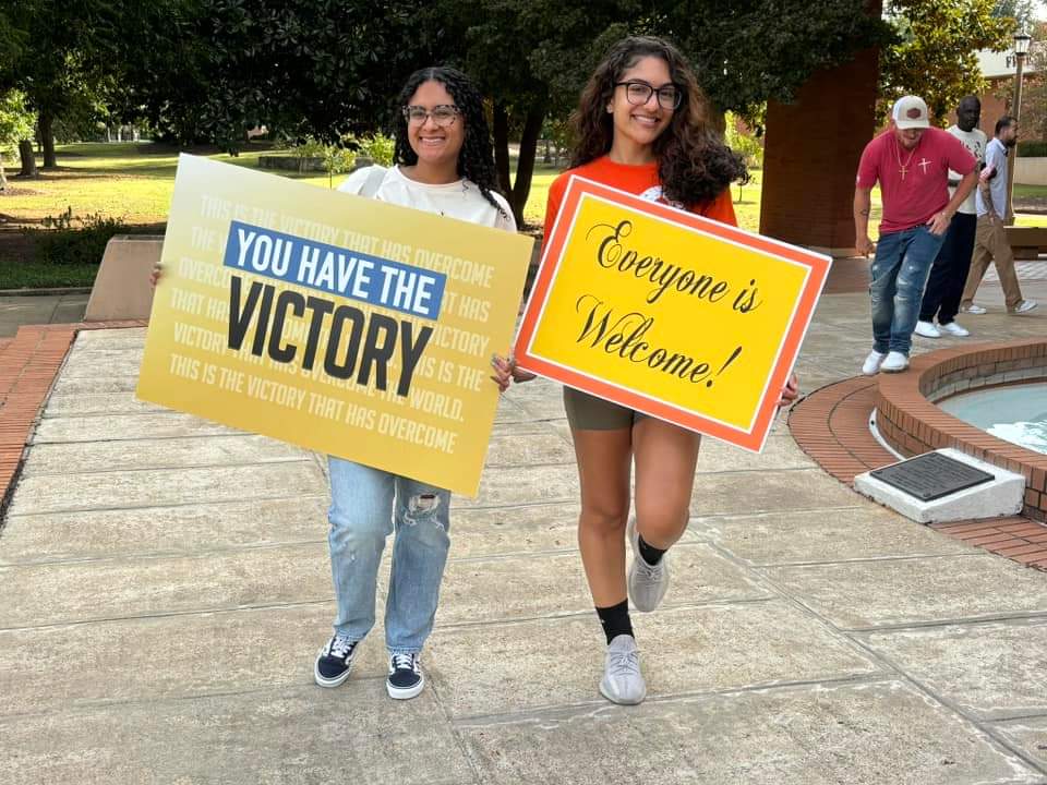 Students holding welcome signs at a church outreach moment.